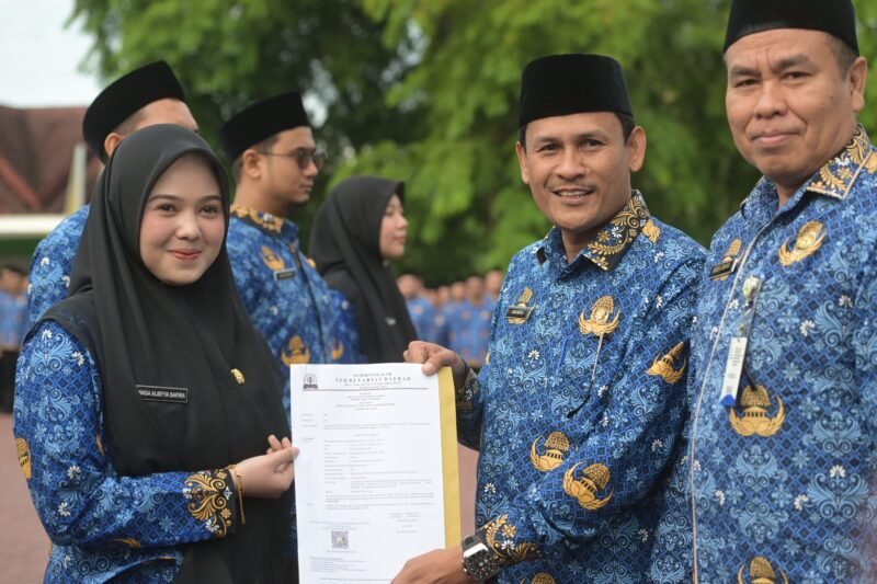 Banda Aceh - Asisten II Sekda Aceh, Zulkifli, mewakili Gubernur Aceh, menyerahkan Surat Keputusan (SK) Gubernur tentang Pengangkatan 618 Calon Aparatur Sipil Negara (CASN) Pemerintah Aceh Tahun 2024. Penyerahan SK dilakukan dalam sebuah upacara yang berlangsung di Halaman Kantor Gubernur Aceh, Selasa 17 Juni 2025. Foto : Dok. Biro Adpim Setda Aceh