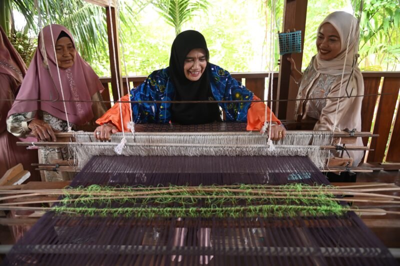 Ketua Dekranasda Aceh Besar Hj. Rita Mayasari menenun kain songket saat berkunjung di Rumah Tenun Mutiara Songket, Gampong Krueng Kalee, Kecamatan Darussalam, Aceh Besar, Sabtu (13/09/2025). FOTO/MC ACEH BESAR