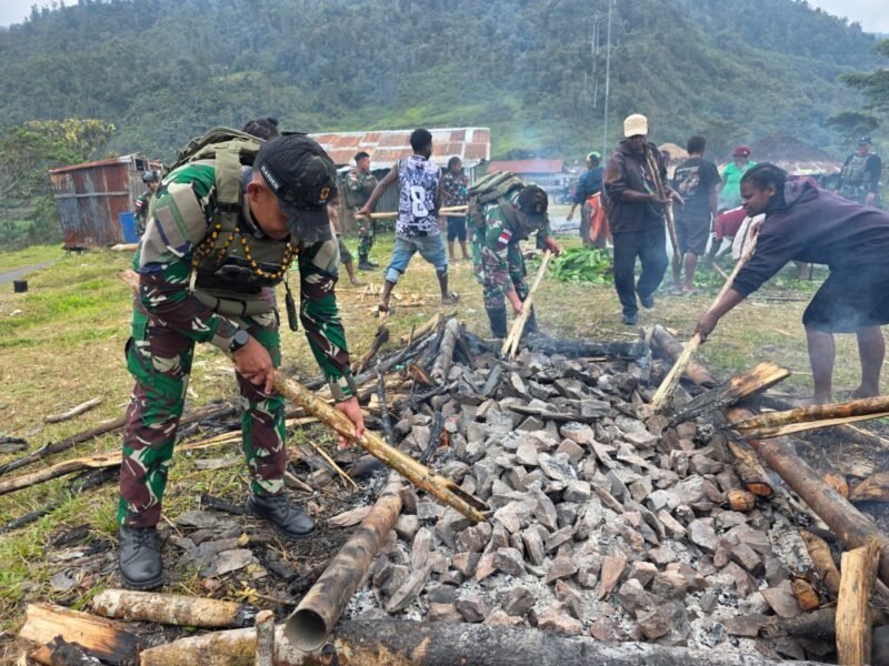 Personel Satgas Yonif 112/DJ bahu-membahu bersama warga Kampung Yarmukum menyiapkan batu panas dalam tradisi Bakar Batu di Distrik Puncak Senyum, Puncak Jaya, Sabtu (10/1/2026).