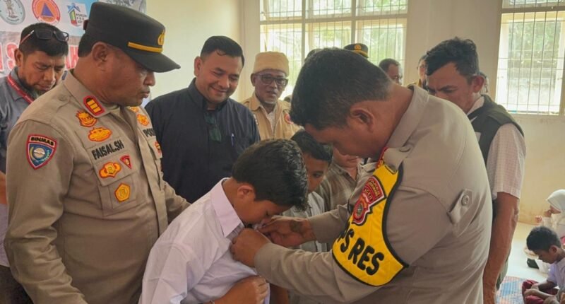 Kapolres Lhokseumawe AKBP Dr. Ahzan memakaikan seragam sekolah kepada siswa SD Negeri 5 Muara Batu saat penyerahan bantuan seragam bersama F-PRB Aceh dan BPBD Bali di Kecamatan Muara Batu, Aceh Utara, Selasa (20/1/2026).