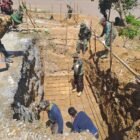 Personel Babinsa Koramil 0108-03/Badar dan Posramil Darul Hasanah bersama warga Desa Kumbang Jaya bahu-membahu memasang rangka pondasi jembatan gantung perintis di Kecamatan Badar, Aceh Tenggara, Minggu (12/4/2026).