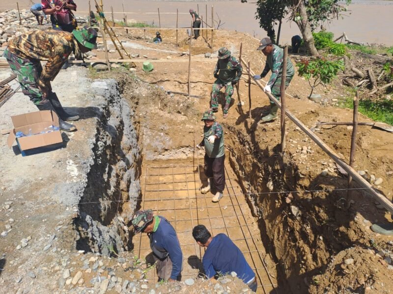 Personel Babinsa Koramil 0108-03/Badar dan Posramil Darul Hasanah bersama warga Desa Kumbang Jaya bahu-membahu memasang rangka pondasi jembatan gantung perintis di Kecamatan Badar, Aceh Tenggara, Minggu (12/4/2026).