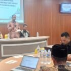 Kepala Biro Pemerintahan dan Otonomi Daerah Setda Aceh, Dr. Bob Mizwar, SSTP, M.Si., saat membacakan sambutan Sekretaris Daerah Aceh pada pembukaan Lokakarya dan Bimtek Pemenuhan SPM Pascabencana Regional I di Lhokseumawe, Kamis (21/5/2026).