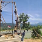 Personel Babinsa Kodim 0108/Aceh Tenggara bersama warga Desa Kumbang Jaya, Kecamatan Badar, bergotong-royong menegakkan tiang pylon Jembatan Gantung Perintis, Senin (01/06/2026).