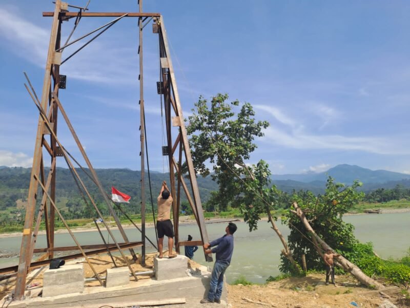 Personel Babinsa Kodim 0108/Aceh Tenggara bersama warga Desa Kumbang Jaya, Kecamatan Badar, bergotong-royong menegakkan tiang pylon Jembatan Gantung Perintis, Senin (01/06/2026). 