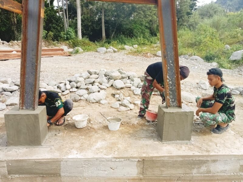 Personel Babinsa Posramil Lawe Sumur Kodim 0108/Aceh Tenggara bersama warga Desa Teger Miko bahu-membahu melakukan pemlesteran pondasi menara pylon Jembatan Gantung Perintis, Selasa (9/6/2026).