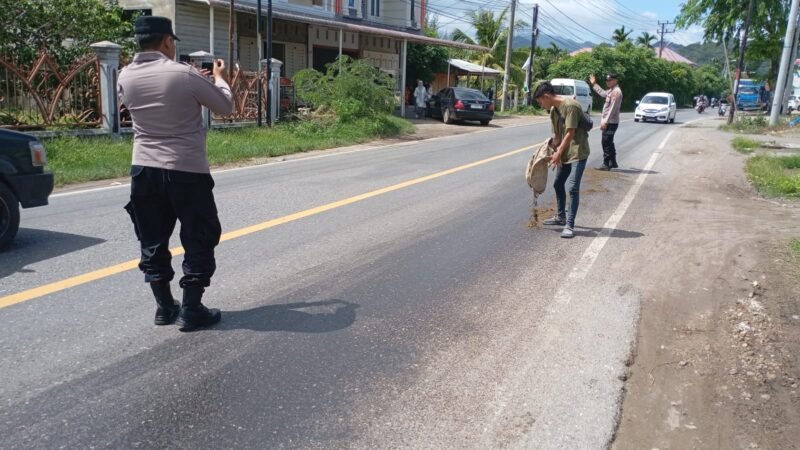 Sejumlah personel Polsek Lhoknga bersama warga bahu-bahu menaburkan pasir di atas tumpahan oli CPO di Jalan Nasional depan BSI Lhoknga, Aceh Besar, Minggu (5/7/2026).