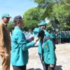 Staf Ahli Bupati Aceh Besar, Fata Muhammad SPd MM memasang topi kepada Mahasiswa KKN USK kepada di halaman Dekranasda, Gampong Gani, Kecamatan Ingin Jaya, Aceh Besar, Selasa (07/07/2026). FOTO/MC ACEH BESAR