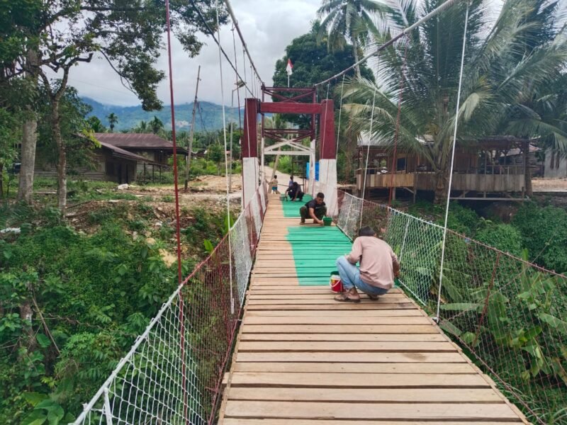Babinsa Kodim 0108/Aceh Tenggara, Serma Zulkifli, bersama warga Desa Kuning Abadi mengecat tiang pylon dan lantai Jembatan Gantung Perintis yang telah mencapai progres 95,5 persen di Kecamatan Ketambe, Aceh Tenggara, Selasa (4/8/2026).