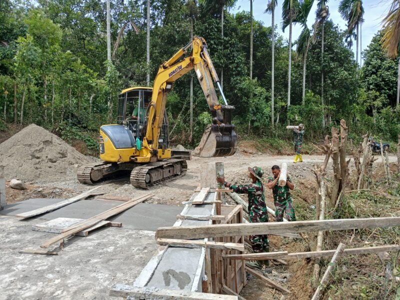 Personel Satgas TMMD Reguler ke-129 Kodim 0102/Pidie bersama alat berat mini excavator mempercepat pemancangan cerucuk kayu dan pohon kelapa/pinang sebagai penahan bantaran jalan pada pembangunan jembatan Box Culvert di Desa Lhok Panah, Kecamatan Sakti, Kabupaten Pidie, Jumat (7/8/2026).