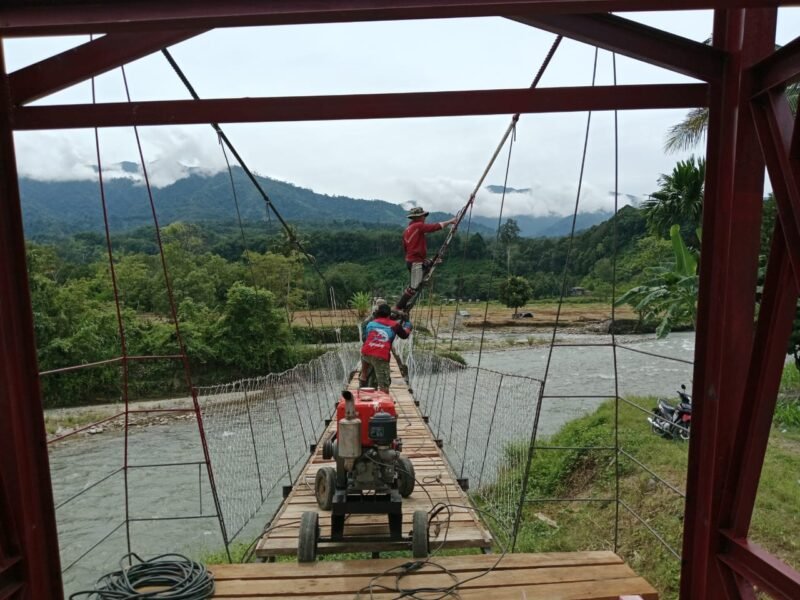 Personel Babinsa Kodim 0108/Aceh Tenggara, Yon TP 855/RD, dan warga setempat bergotong royong memasang tiang hanger pada pembangunan Jembatan Gantung Perintis di Desa Kuta Ujung, Kecamatan Darul Hasanah, Aceh Tenggara, Sabtu (8/8/2026).
