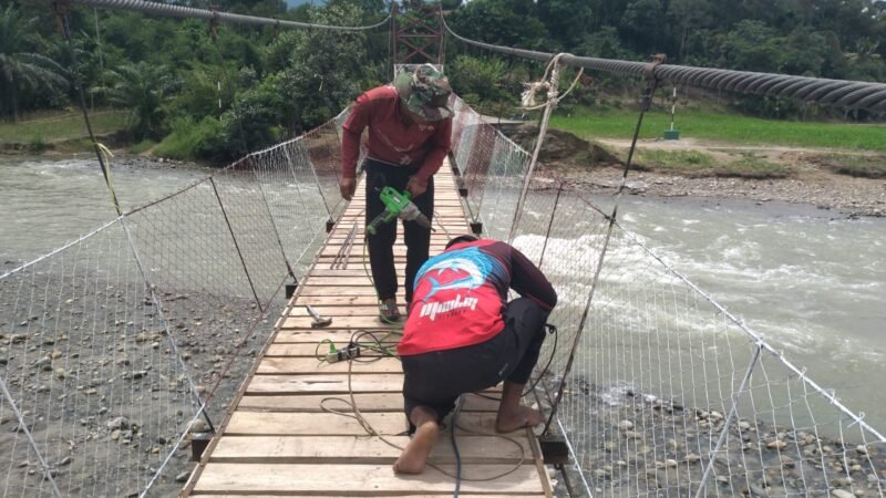 Personel Babinsa Kodim 0108/Aceh Tenggara bersama tim teknis dan warga Desa Gulo, Kecamatan Darul Hasanah, bahu-membahu memasang hanger (pengait) dan papan lantai pada pembangunan Jembatan Gantung Perintis, Kamis (20/8/2026).