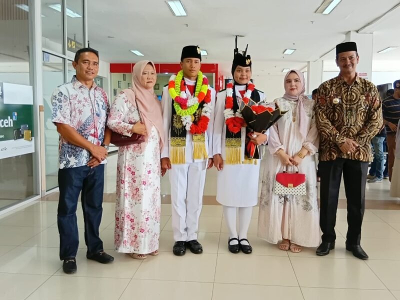 Camat Kuta Baro Zahrul Fuadi SE MM menyambut kepulangan Muhammad Hibban Annafis, anggota Paskibraka Nasional asal Gampong Cot Cut, di Bandara Sultan Iskandar Muda, Sabtu (22/8/2026).