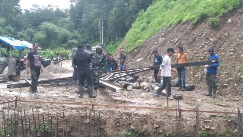Babinsa Kodim 0108/Aceh Tenggara bersama warga bergotong royong mengangkat dan menyeberangkan material tiang pylon untuk pembangunan Jembatan Gantung Perintis di Desa Kuta Ujung, Kecamatan Darul Hasanah, Aceh Tenggara, Selasa (27/10/2026). Foto: NA