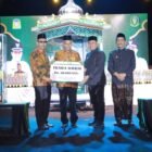 Bupati Aceh Besar H. Muharram Idris menyerahkan hadiah uang pembinaan kepada Peukan Bada setelah menjadi juara umum MTQ ke-35 Tingkat Kabupaten Aceh Besar malam penutupan, di arena utama, Lapangan Kemukiman Bung Cala, Kecamatan Kuta Baro, Jumat (30/10/2026). Foto: Prokopim Aceh Besar