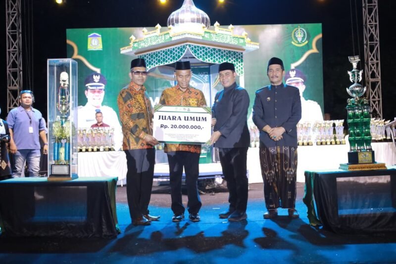 Bupati Aceh Besar H. Muharram Idris menyerahkan hadiah uang pembinaan kepada Peukan Bada setelah menjadi juara umum MTQ ke-35 Tingkat Kabupaten Aceh Besar malam penutupan, di arena utama, Lapangan Kemukiman Bung Cala, Kecamatan Kuta Baro, Jumat (30/10/2026). Foto: Prokopim Aceh Besar